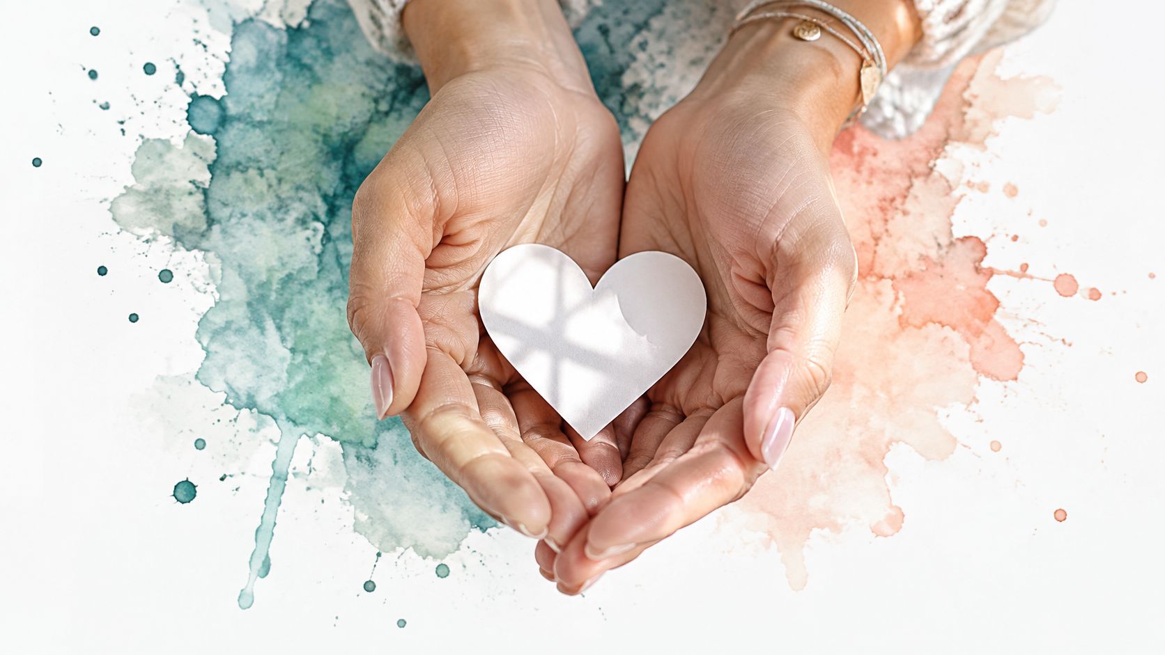 A person gently cupping a white paper heart in their hands against a colorful watercolor background.